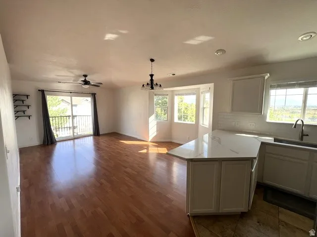 Spacious open-concept living area featuring wood-finish flooring, a ceiling fan, and multiple windows