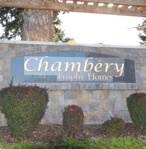 Stone-clad entry monument featuring an integrated sign, decorative plantings, and a wooden arbor overhead