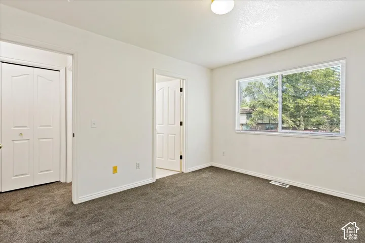 White walls with dark gray carpeting, featuring a window with horizontal blinds, and two interior doors