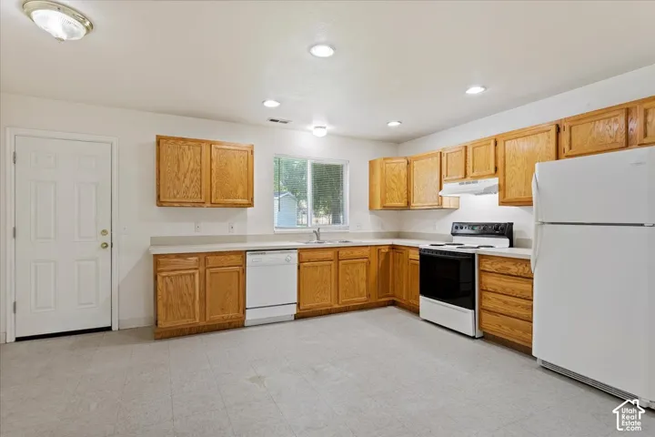 Kitchen featuring wood cabinetry, white appliances, recessed lighting, and a window above the sink