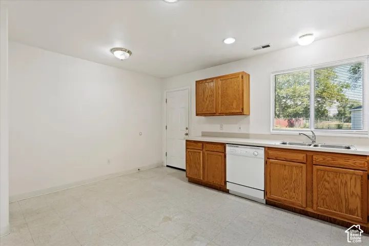 White appliances, wood cabinetry, dual basin stainless steel sink, large window, and recessed lighting