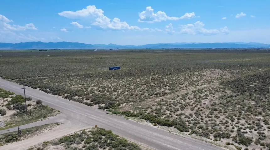 Expansive undeveloped land featuring natural desert vegetation, a gravel road, and distant mountain ranges