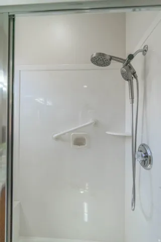 Walk-in shower enclosure featuring a built-in shower shelf and grab bar and easy to clean cultured marble