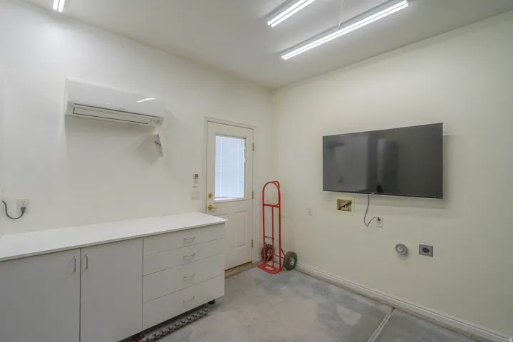 Built-in white cabinetry with a solid surface countertop, glass-paneled door, and exposed utility hookups. Mini-split provides heat and air conditioning