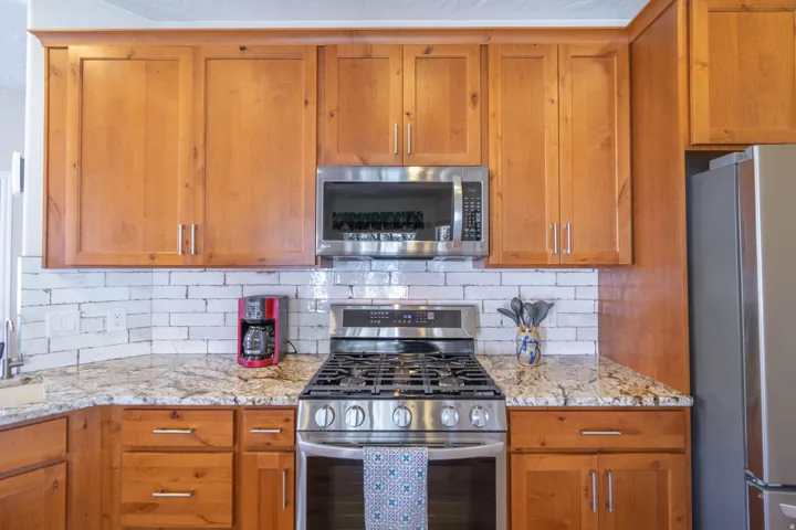 Updated wood-finish cabinetry paired with stainless steel appliances, a gas range, light subway tile backsplash, and granite countertops