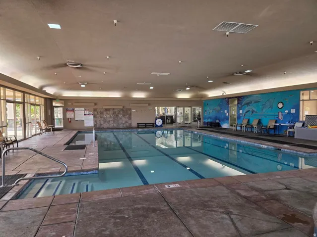Indoor lap pool with integrated hot tub, surrounded by extensive window walls and a decorative mural