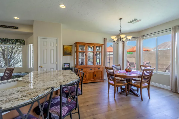 Curved granite countertop peninsula, recessed lighting, wood-finish LVP flooring, large bay windows, and a five-light chandelier