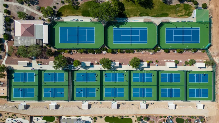 Multiple tennis courts and pickleball courts with paved pathways and mature landscaping