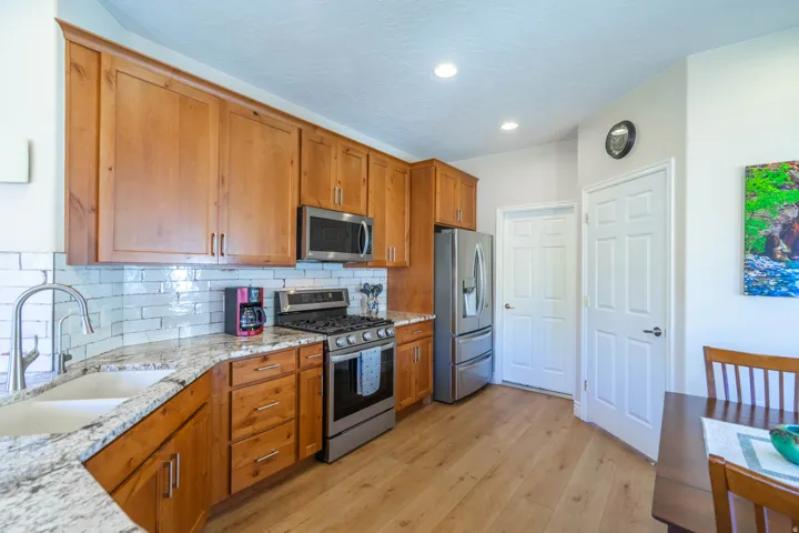 Kitchen featuring updated wood cabinetry, light-toned granite countertops, a white subway tile backsplash, stainless steel appliances, and wood-finish LVP flooring