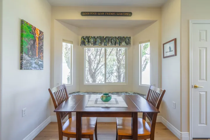 Eat in kitchen with bay window with integrated bench seating, LVP wood-finish flooring, and a paneled door with brass hardware that is the pantry