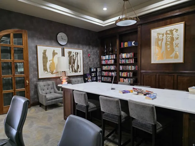 Library with Built-in wood cabinetry, coffered ceiling, and a central island with a light-toned countertop and comfortable seating