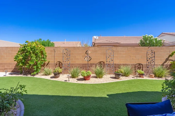 Artificial turf lawn with a curved edge, surrounded by a gravel bed featuring potted plants and various greenery