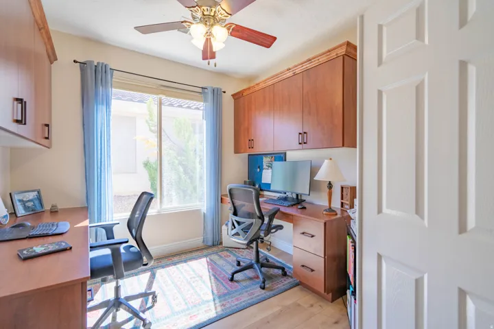 Built-in wood-finish cabinetry, wood-finish desk with drawers, ceiling fan light fixture, and wood-finish flooring