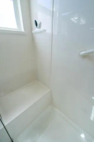Shower stall with a built-in bench, integrated shelving, and a grab bar