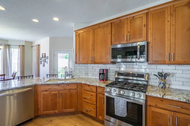 Full-height wood cabinetry with stainless steel hardware, white subway tile backsplash, stainless steel appliances, and light-toned LVPwood-finish flooring