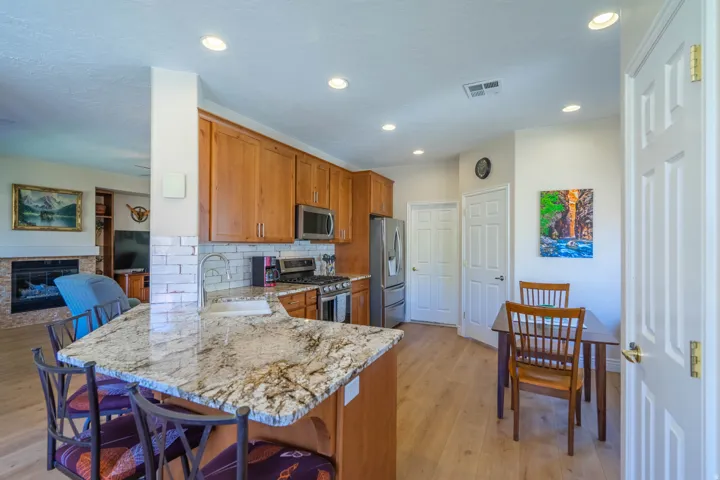 Kitchen with a breakfast bar featuring a granite countertop, wood cabinetry, stainless steel appliances, and wood-finish flooring