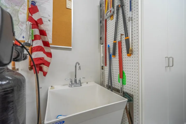 Utility sink with chrome faucet, white storage cabinetry, and pegboard wall storage