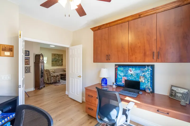 Wood-finish flooring, built-in wooden desk, built-in wooden cabinetry with crown molding, ceiling fan, and paneled interior door