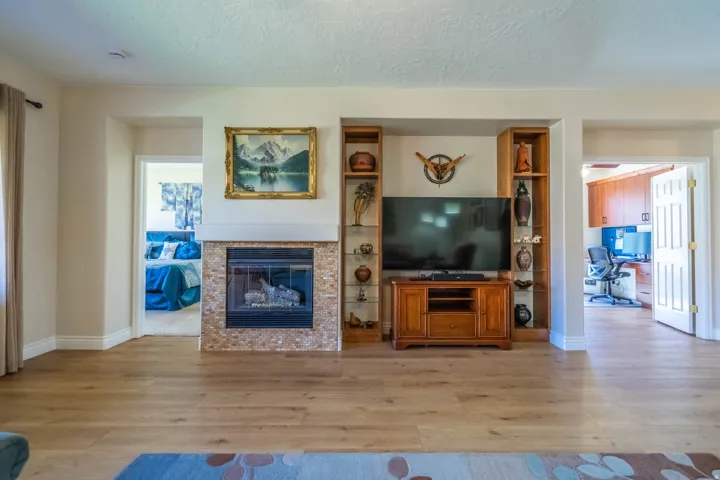 Wood-finish flooring, built-in entertainment center with shelving, and a fireplace featuring a tiled surround. Primary bedroom on left and den on right.