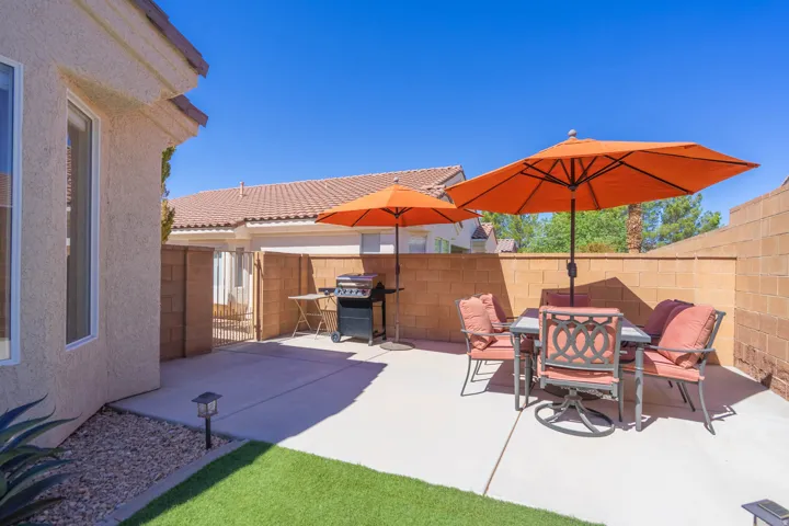 Paved patio area, stucco exterior, block wall fencing, low-maintenance artificial turf, and a gated access point