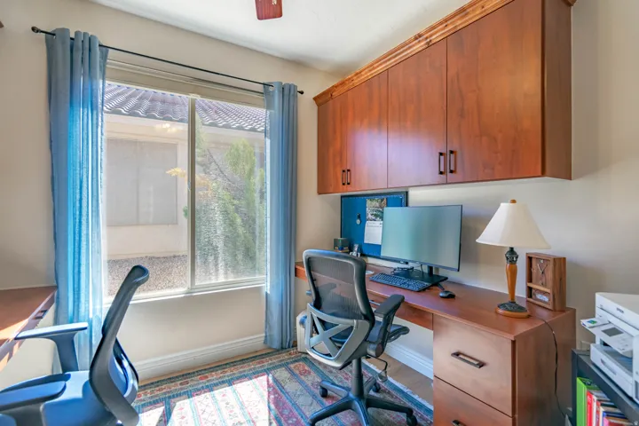 Built-in wood cabinetry with crown molding, wood-finish desk, and a window with light-filtering curtains