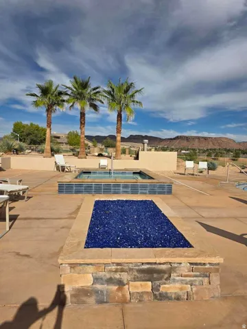 Stone-clad fire pit with blue glass media, concrete patio, and in-ground spa with blue glass tile surround
