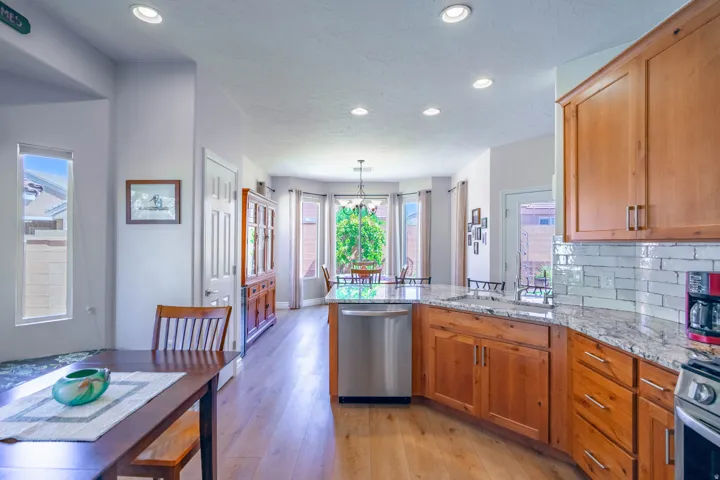 Open kitchen with wood-finish flooring, recessed lighting, wood cabinetry, stainless steel appliances, and a tile backsplash. Eat in kitchen and semi-formal dining beyond