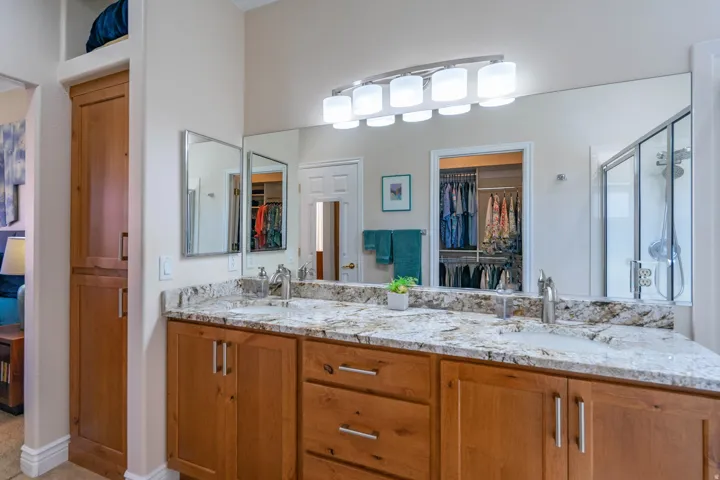 Dual vanity with wood-finish cabinetry, light-toned countertop, under-mount sinks, and a large wall-mounted mirror