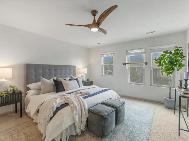 Carpeted bedroom with a wood-finish ceiling fan and three windows