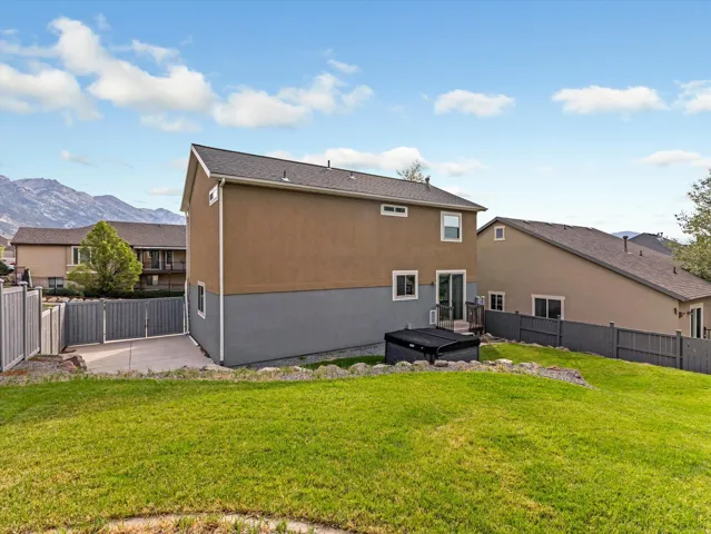 Expansive green lawn, stucco exterior, rear deck, privacy fencing, and mountain scenery