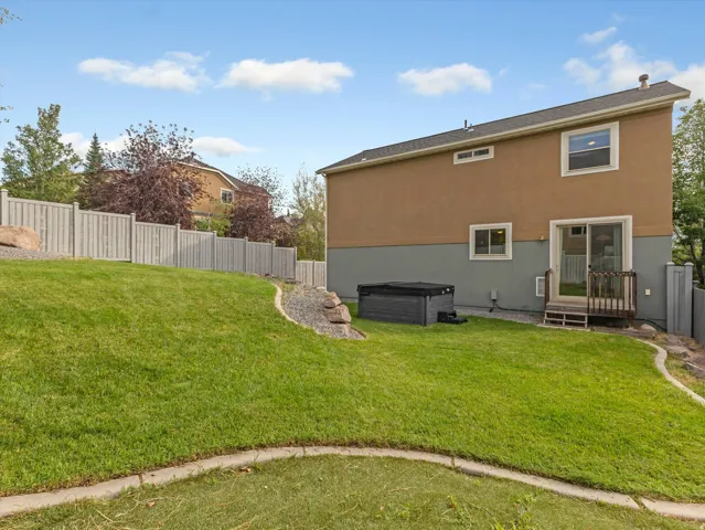 Expansive sloped lawn with a spa, sliding glass door access to the interior, and a wood privacy fence