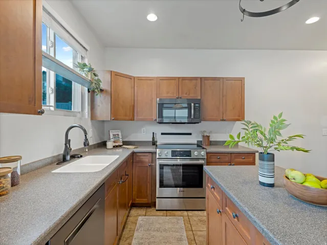 Kitchen featuring wood cabinetry, stainless steel appliances, a white basin sink, and ample countertop space