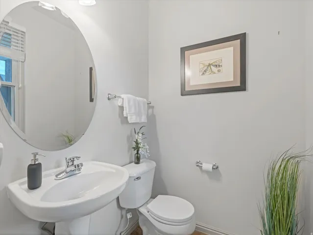 Pedestal sink with chrome faucet, oval mirror, and white toilet
