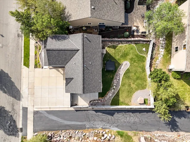 Shingle roof, concrete driveway, stone pathway, lawn, and mature trees