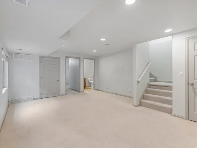 Expansive carpeted area with recessed lighting, a window, and a staircase with a handrail
