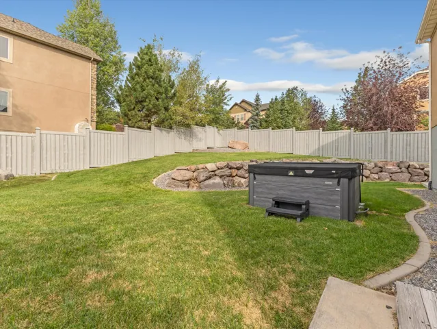 Expansive backyard featuring a hot tub, rock retaining wall, gravel border, and privacy fencing