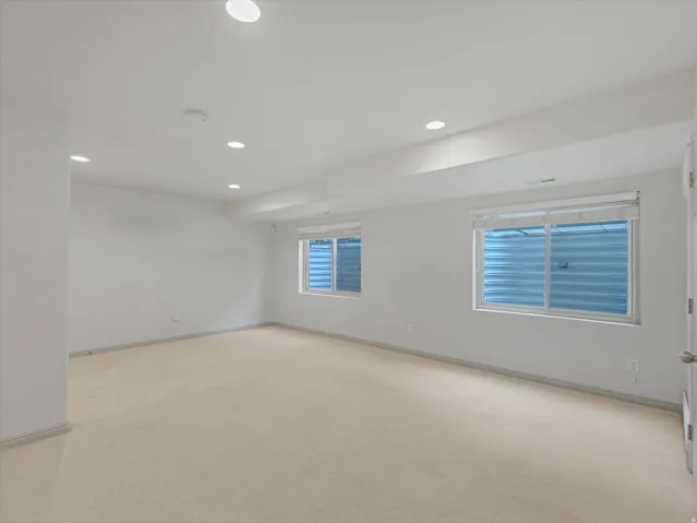Recessed lighting, light-toned carpeting, two windows with blinds, a white paneled door, and neutral-toned wall paint