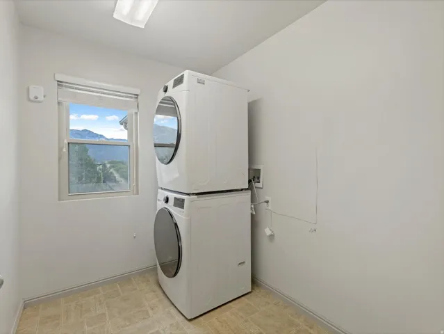 Dedicated laundry room featuring stacked white front-load dryers and washer units, wood-finish flooring, natural light from an opaque window, and neutral wall finishes ideal for efficient household management