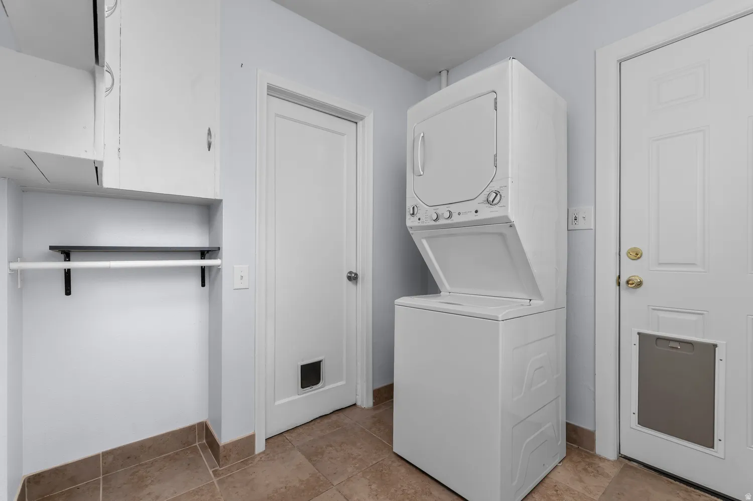Laundry area featuring a stacked washer and dryer, built-in shelving, white cabinetry, and durable tile flooring