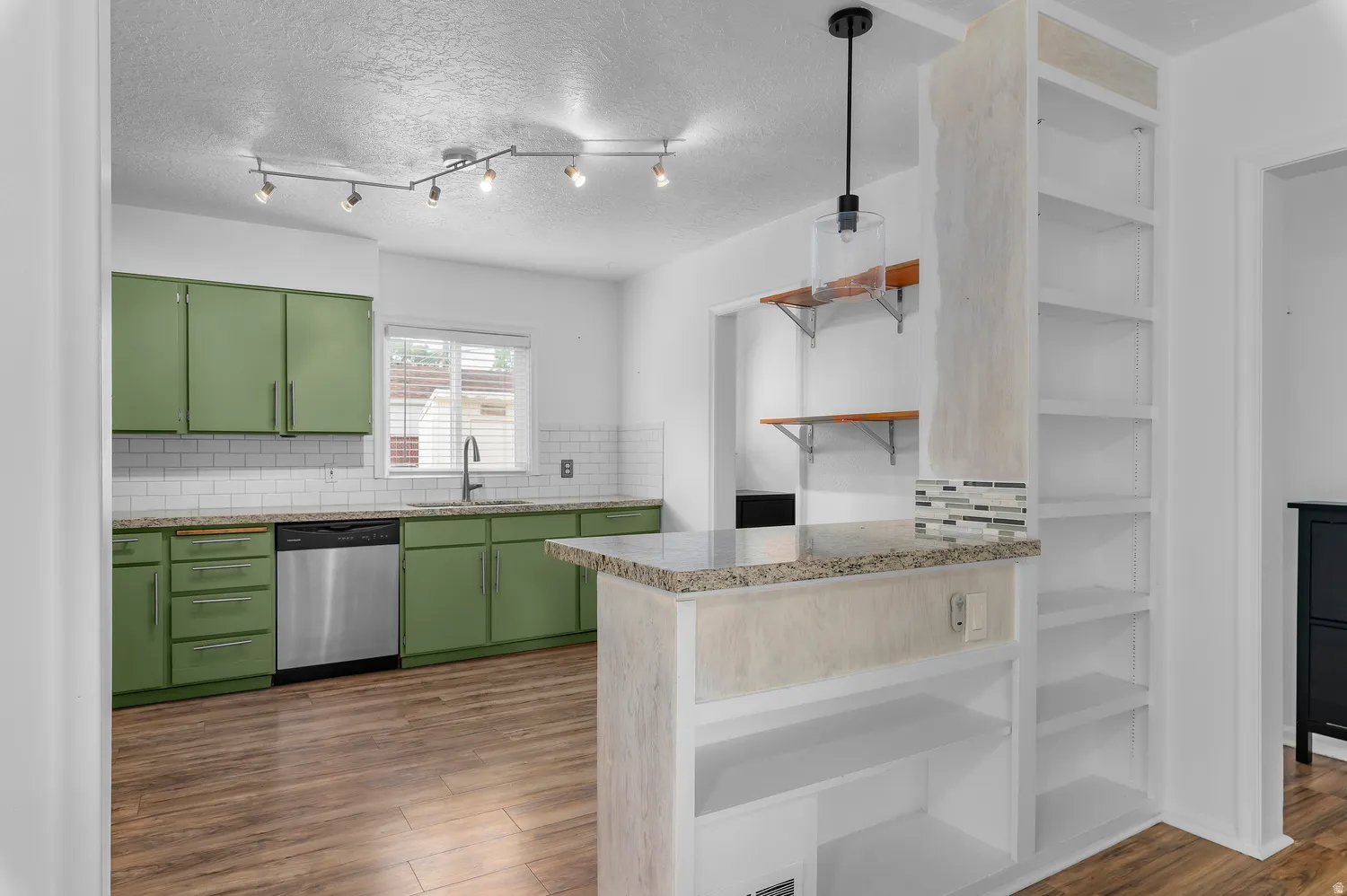 Kitchen featuring wood-finish flooring, green cabinetry, white subway tile backsplash, and stainless steel dishwasher