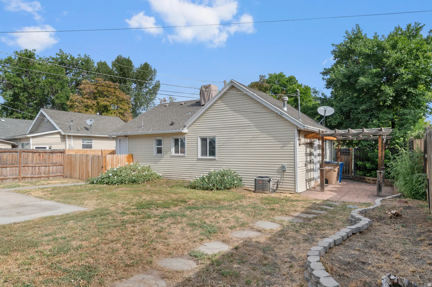 Spacious backyard featuring a paver patio, wood pergola, raised garden bed, and stone pathway