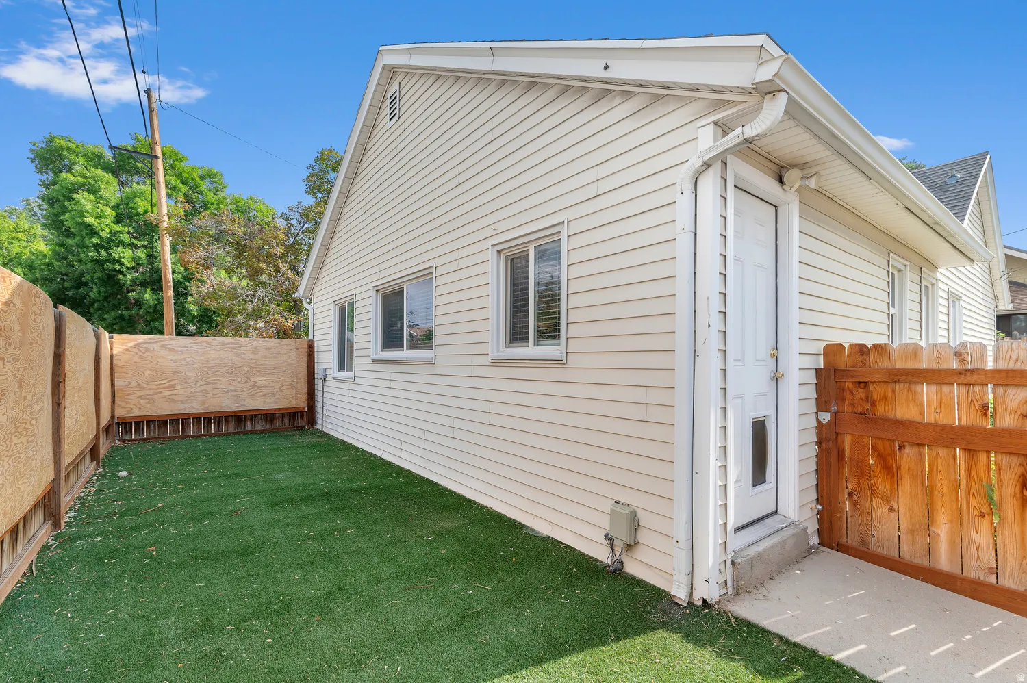 Exterior siding, white-trimmed windows, fenced yard with artificial turf, and a side entry door