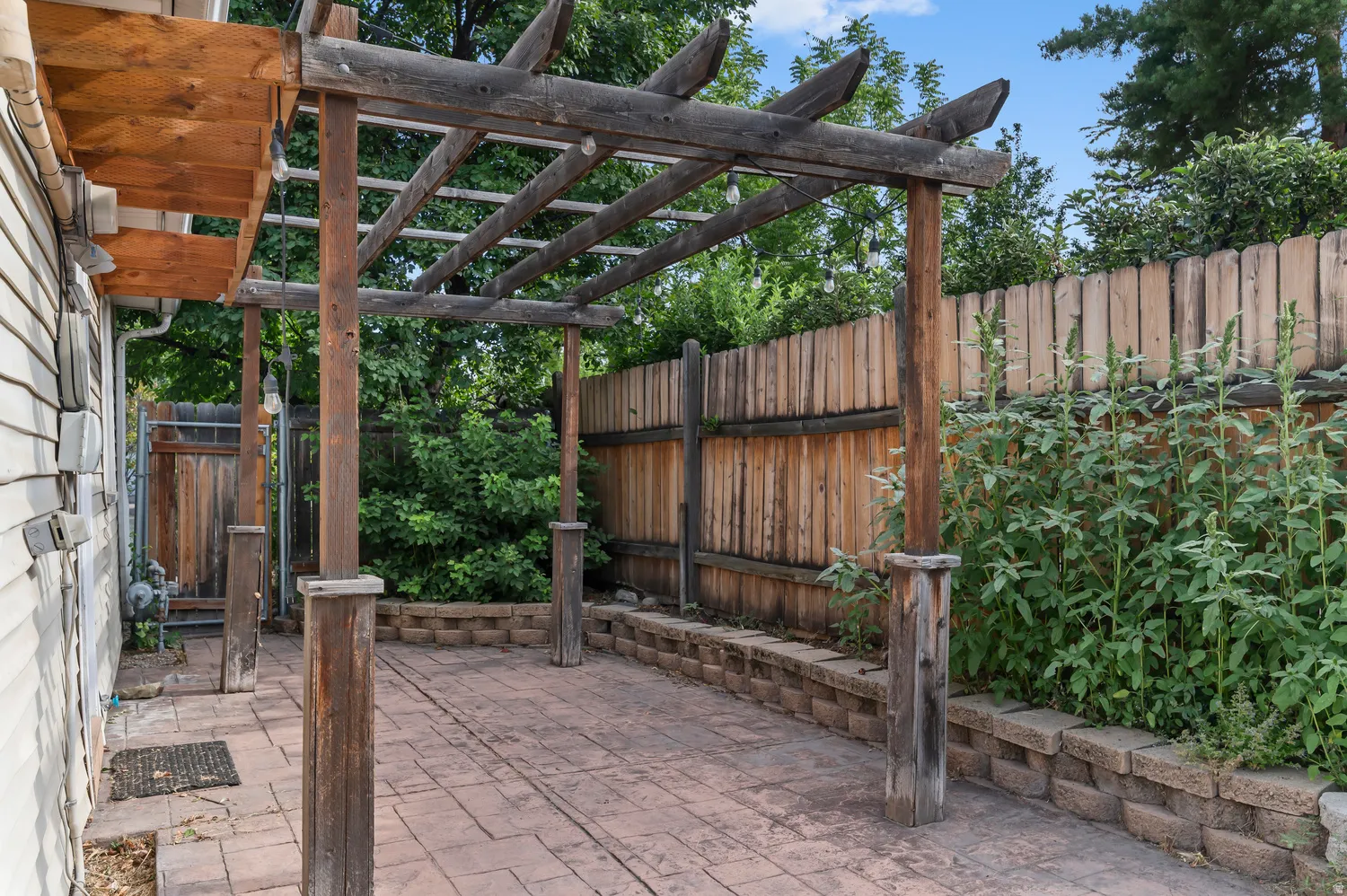 Covered patio with rustic wood-beam pergola structure, clay brick paver flooring, and wooden privacy fencing