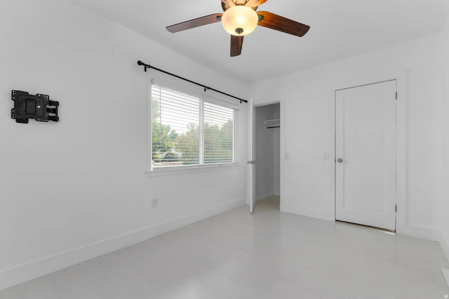 White painted walls, white flooring, window with blinds, ceiling fan with light fixture, and a built-in closet with shelving