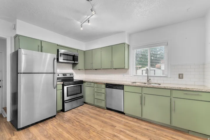 Kitchen featuring wood-finish flooring, stainless steel appliances, white subway tile backsplash, light-toned countertops, and green cabinetry