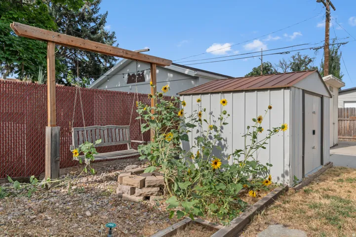 Backyard space featuring a storage shed with a brown metal roof, wood garden beds, and a wood swing frame