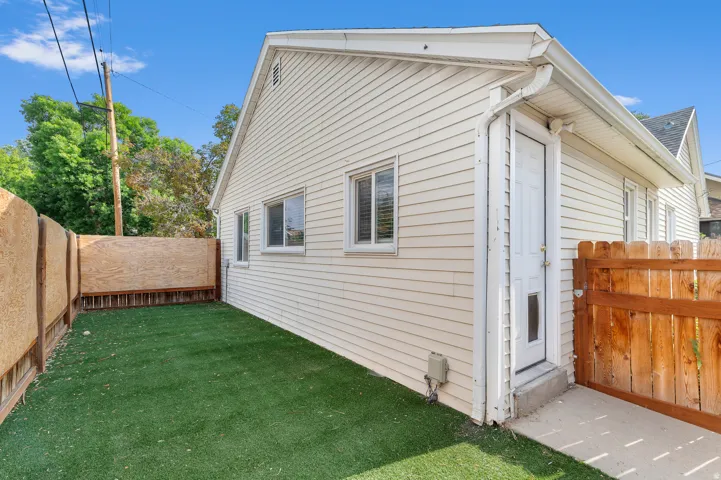 Exterior siding, white-trimmed windows, fenced yard with artificial turf, and a side entry door