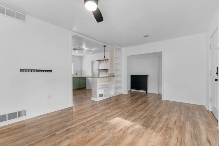 Open-concept living area featuring wood-finish flooring, a ceiling fan, and built-in shelving