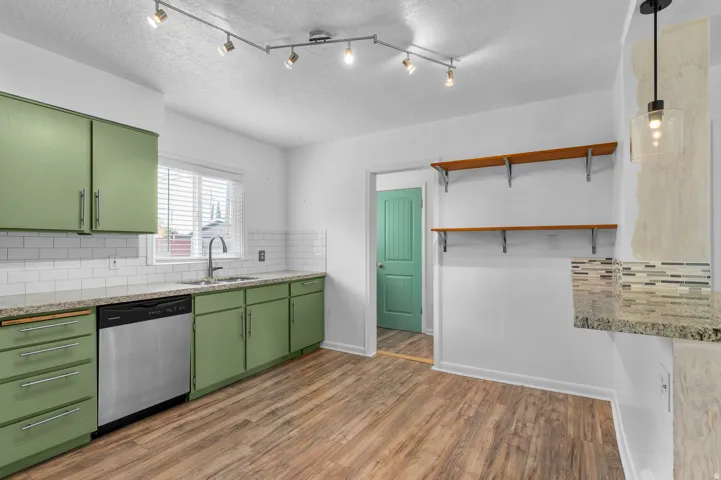 Kitchen featuring green cabinetry, wood-finish flooring, white subway tile backsplash, and stainless steel appliances