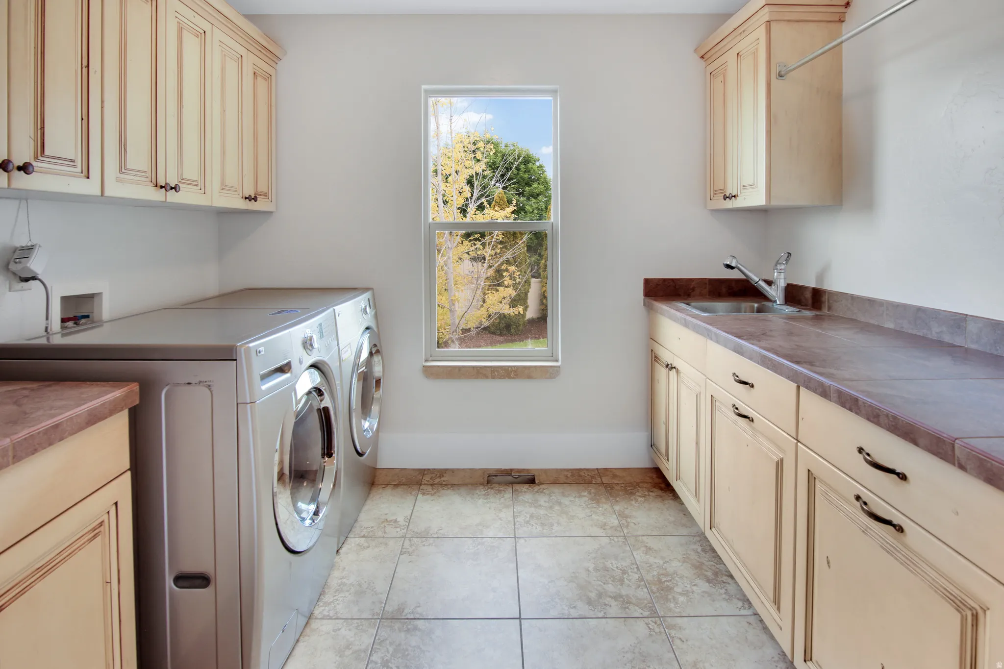 Laundry area featuring tile flooring, built-in cabinetry, a utility sink, and a window